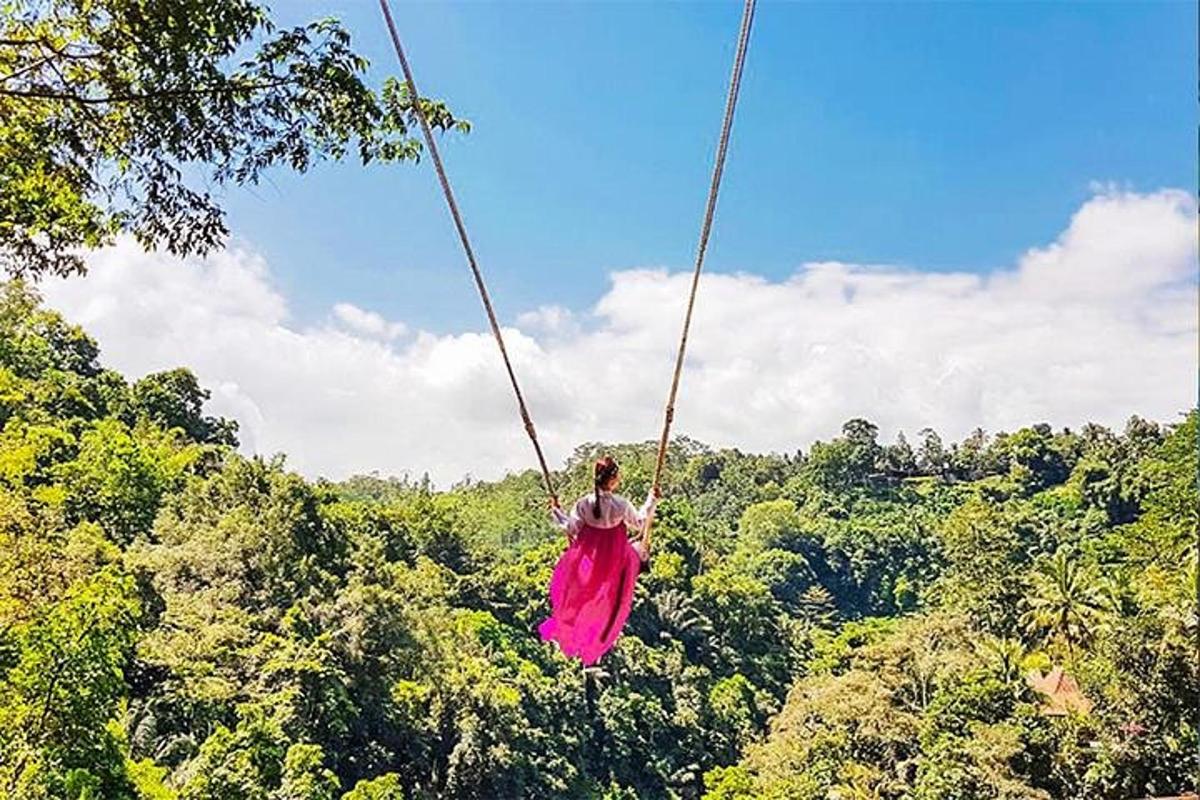 a woman in a pink dress swinging on a rope swing