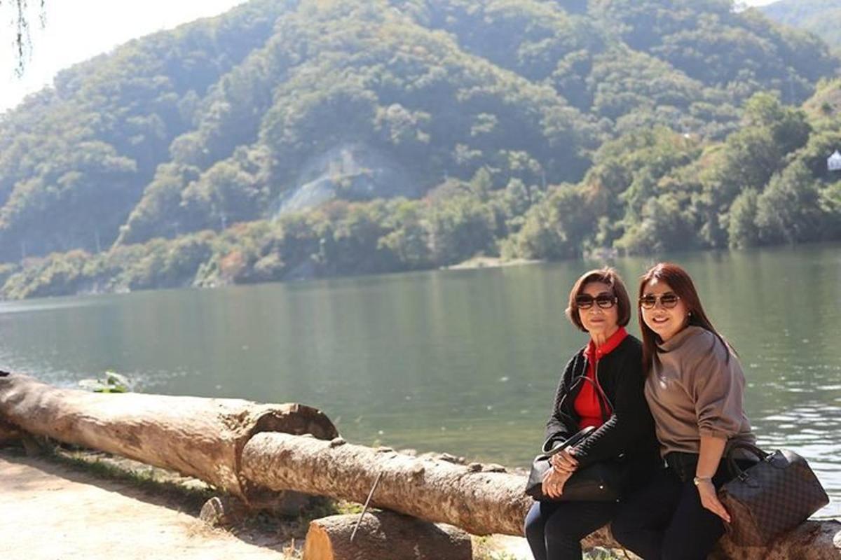 dua wanita duduk di atas batang kayu di dekat danau