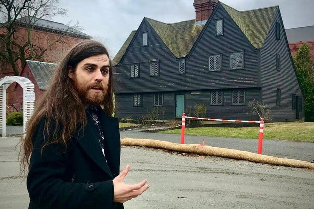 a man with long hair standing in front of a house