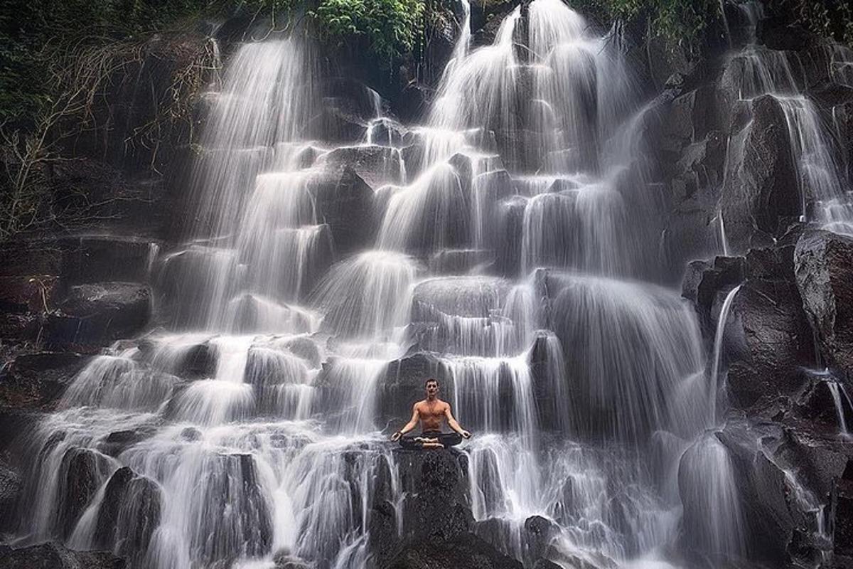 a man sitting on a rock in front of a waterfall