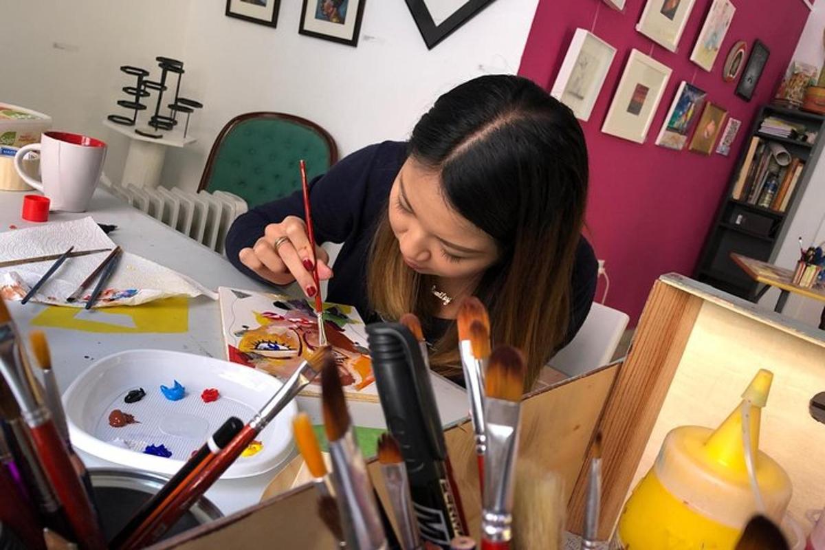a woman sitting at a table painting with paint brushes