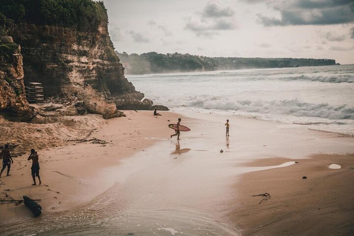 Grupa ludzi spacerujących po plaży z deską surfingową