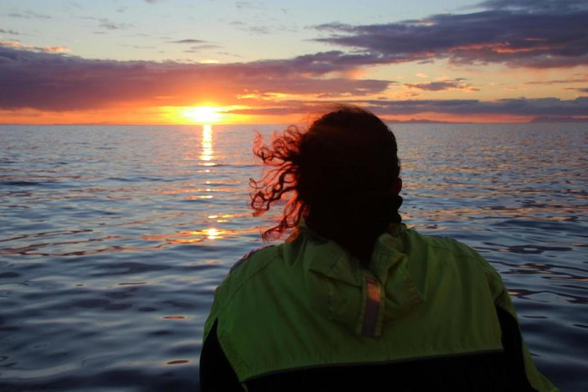 uma pessoa sentada em um barco observando o pôr do sol