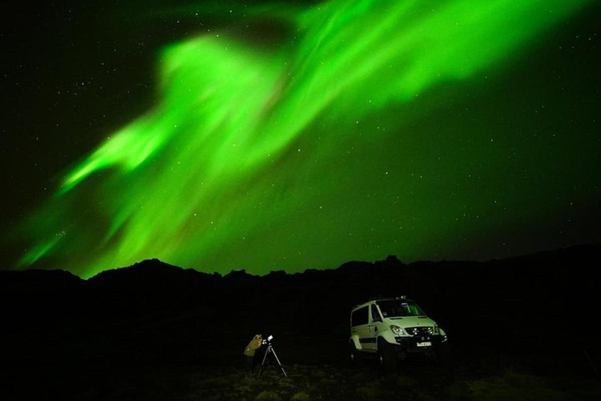 uma pessoa parada em frente a um trailer sob a aurora boreal