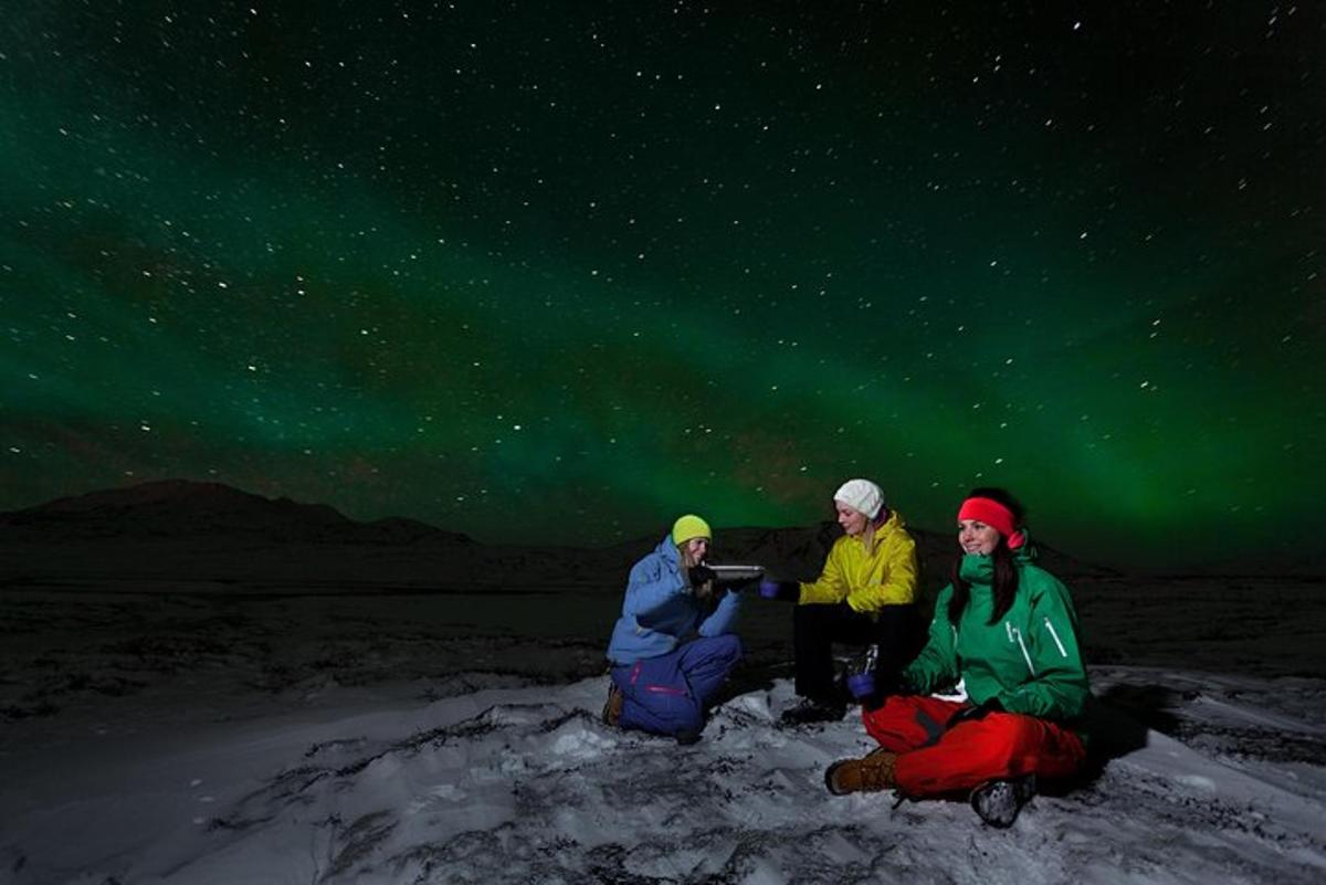 três pessoas sentadas na neve sob as estrelas