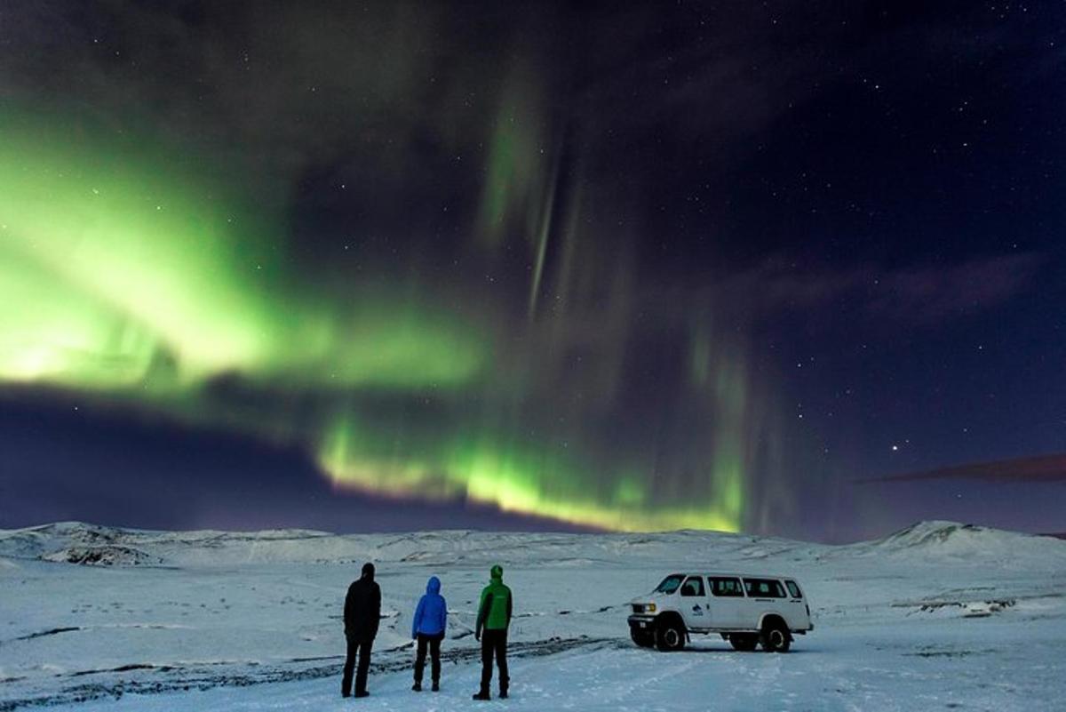 três pessoas em pé ao lado de um carro sob a aurora boreal
