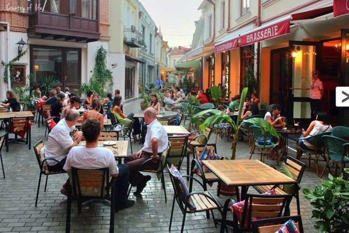 cilvēku grupa, kas sēž pie galdiņiem ārpus restorāna