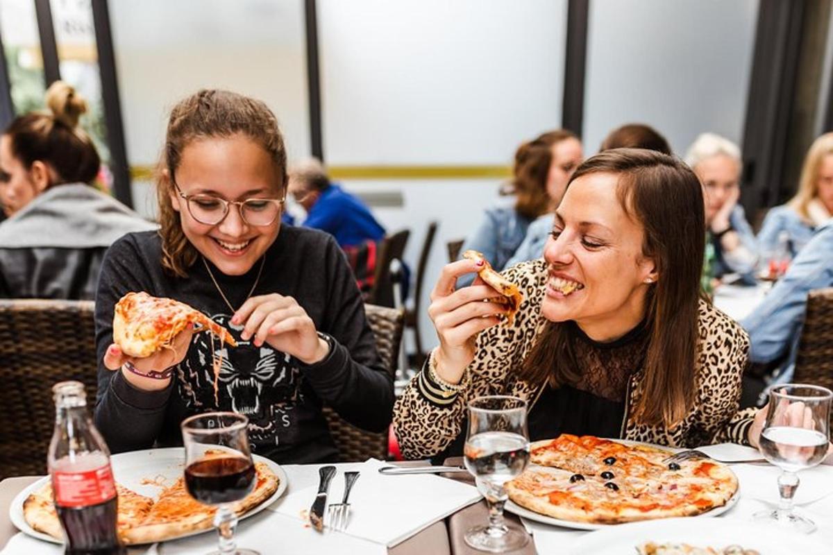 dvě ženy sedící u stolu a jedoucí pizzu