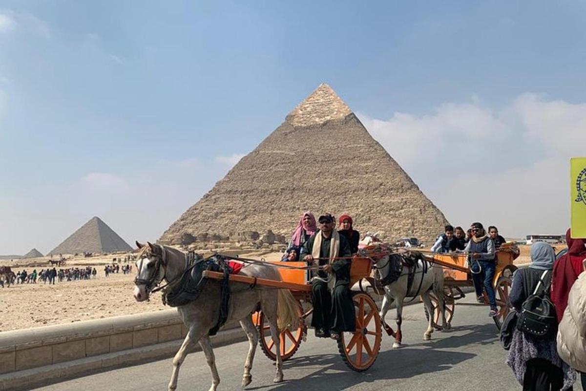 Skupina lidí jedoucích na koňských povozech před pyramidami