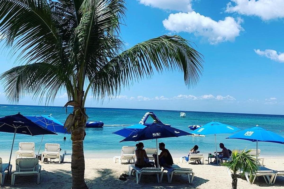 Menschen sitzen an einem Strand mit blauen Sonnenschirmen und dem Meer