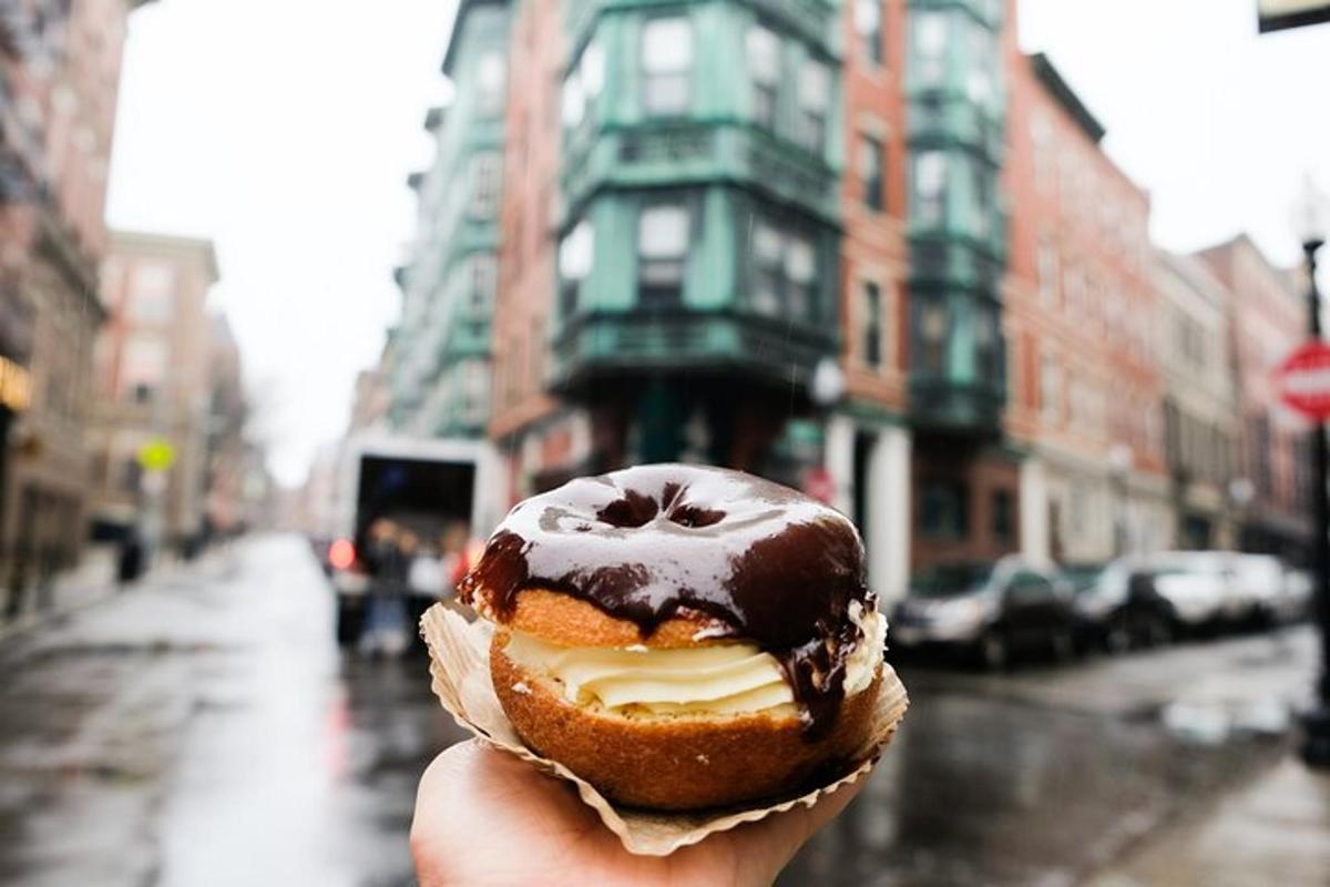 uma pessoa segurando um donut com chocolate em uma rua da cidade