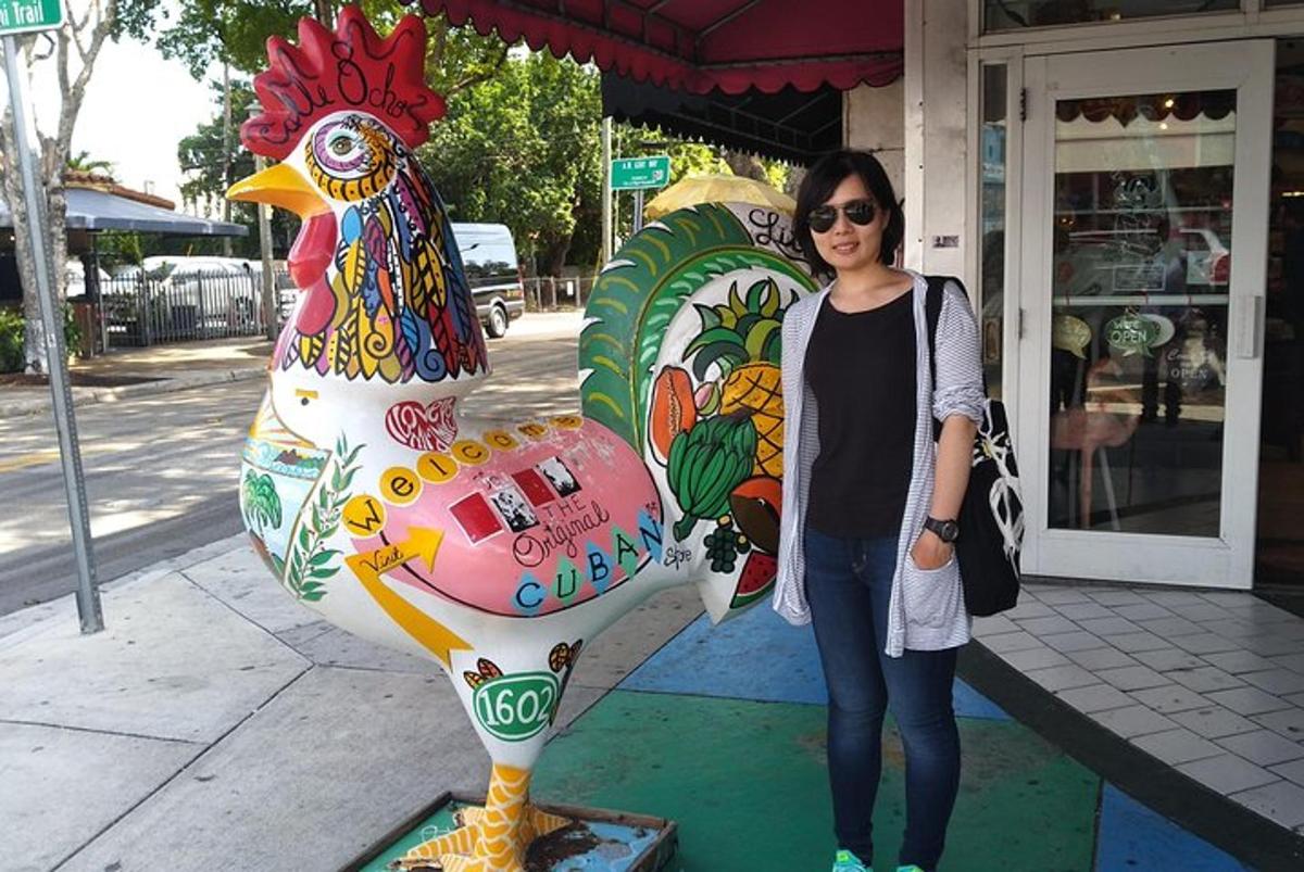 một người phụ nữ đứng cạnh một bức tượng lớn hình con gà