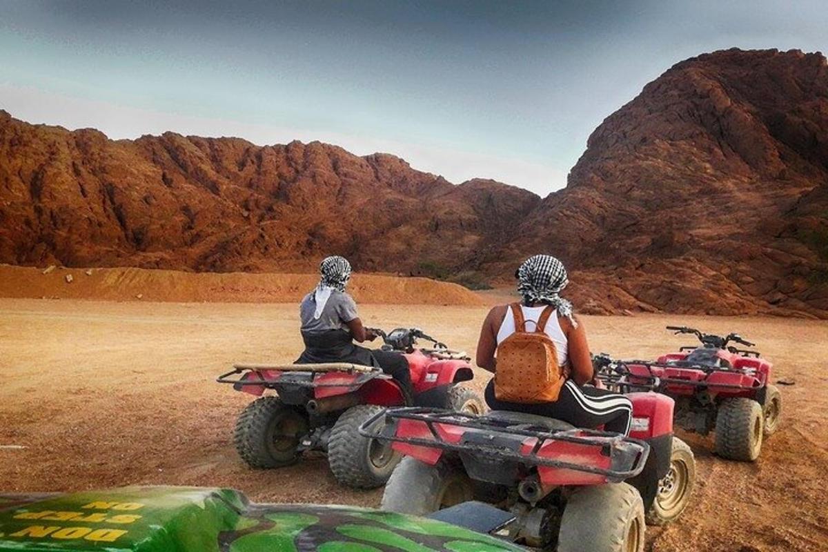 dues persones condueixen quads al desert