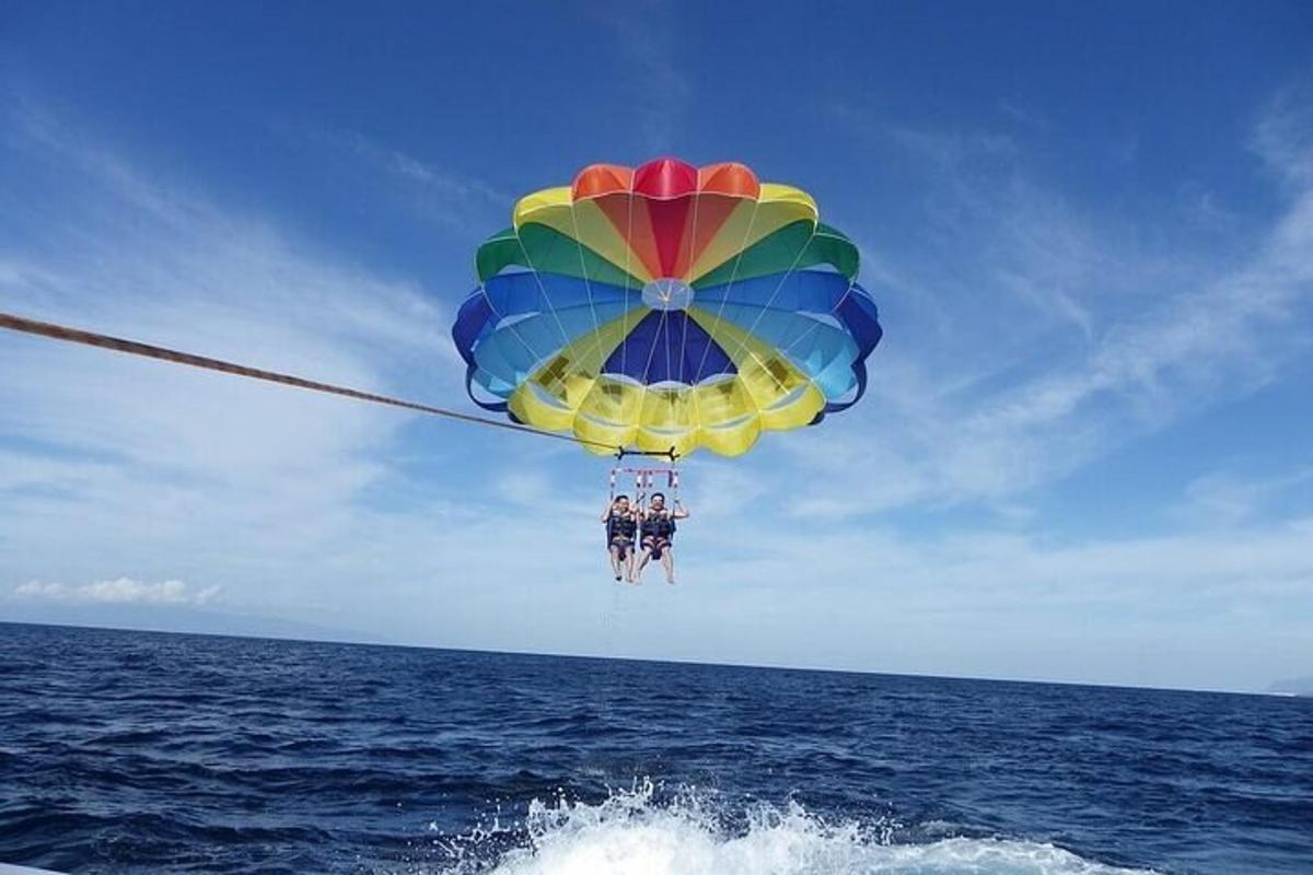 dva lidé visící z barevného deštníku nad oceánem