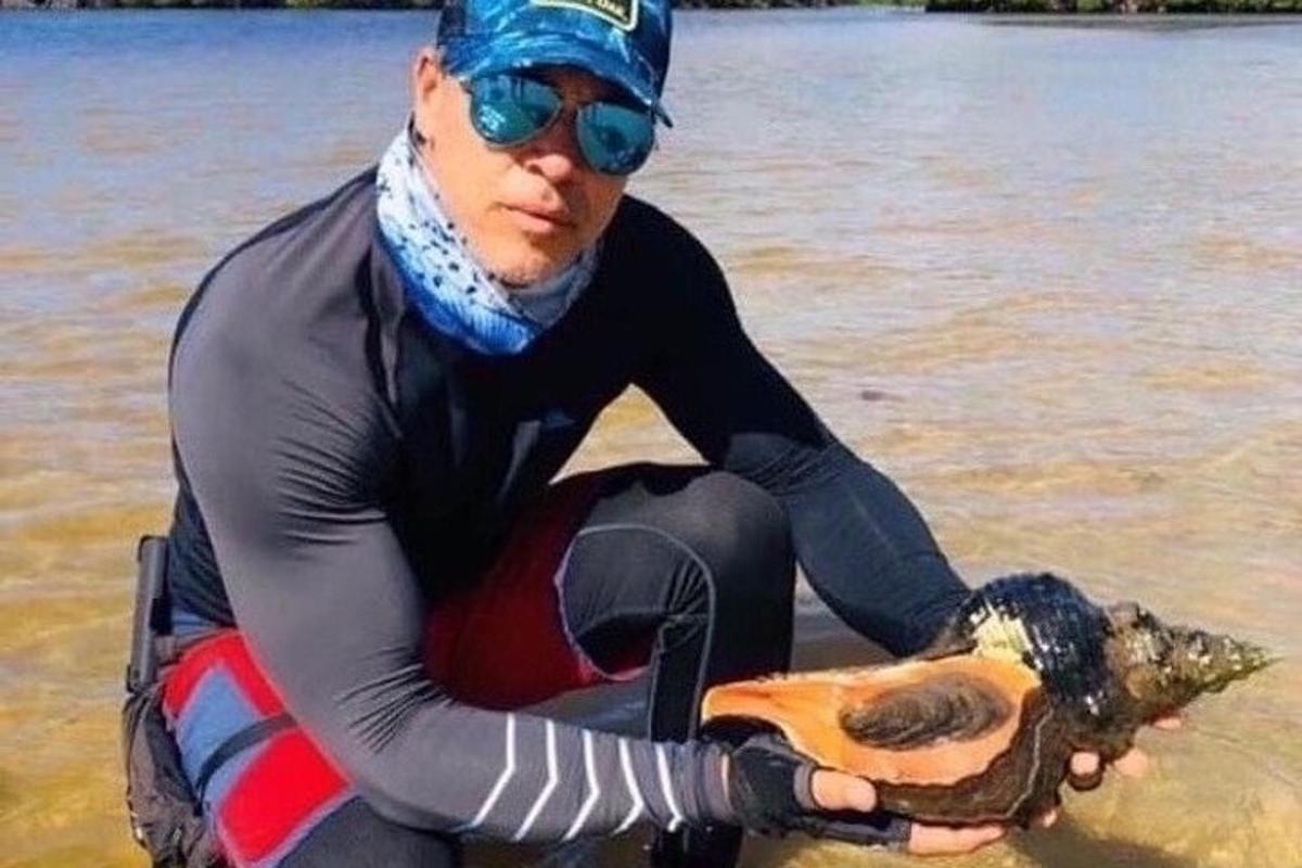 a man in a wetsuit holding a dead animal