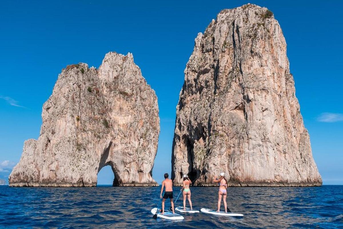 tři lidé na paddleboardech v oceánu s velkým skalním útvarem
