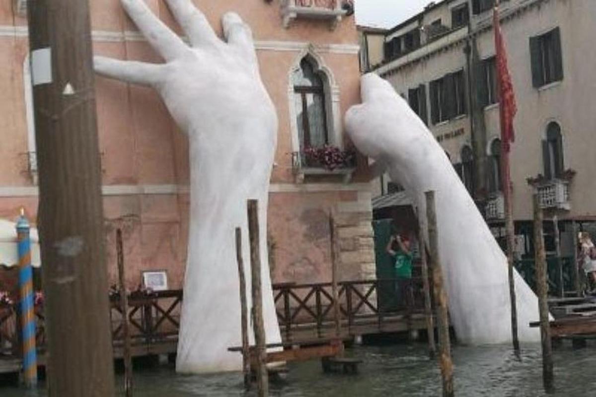 Una estatua de dos manos en el agua junto a un edificio.