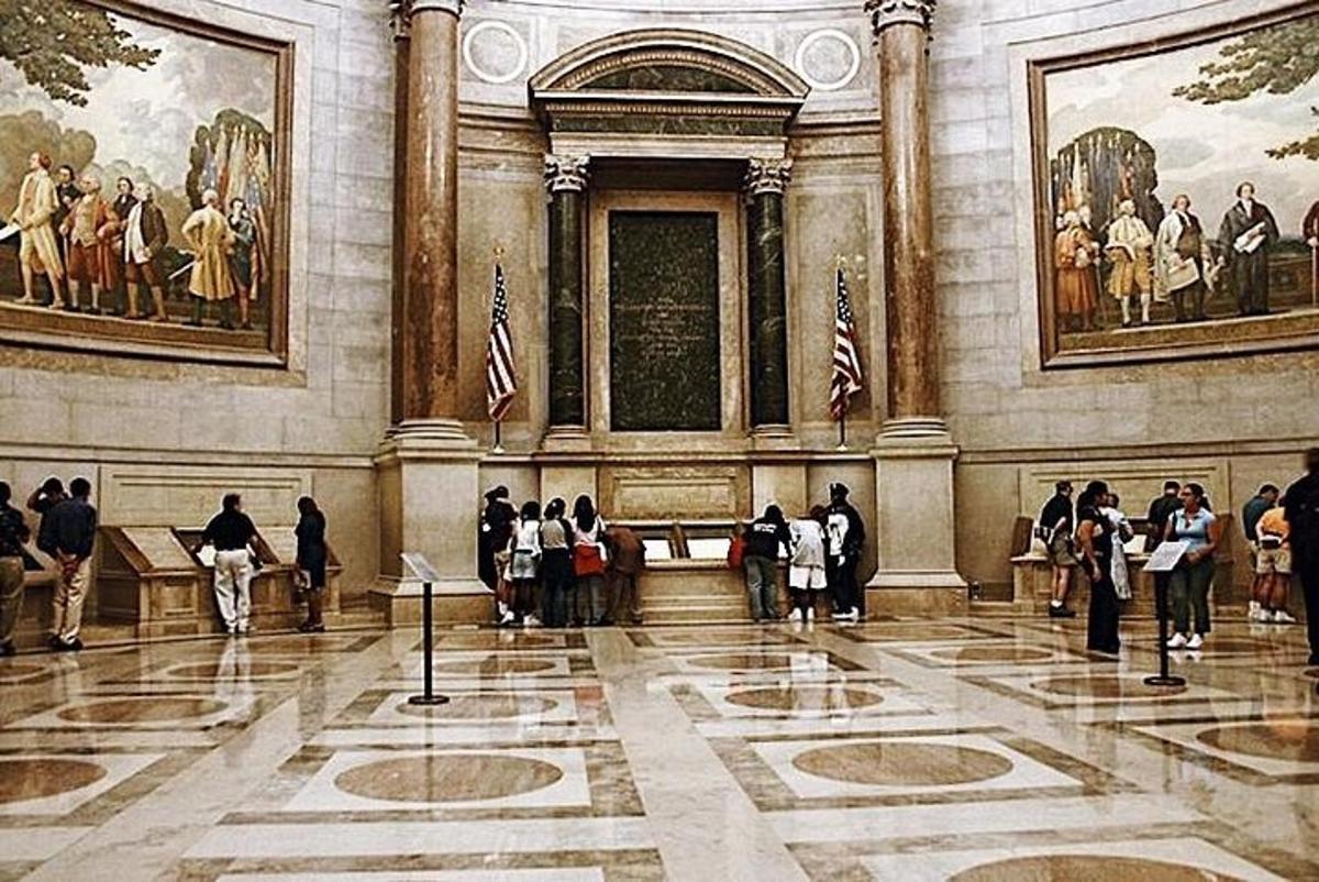 a group of people standing in a large room with paintings