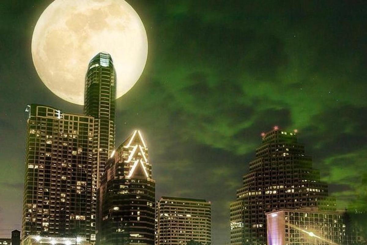 a full moon over a city with tall buildings
