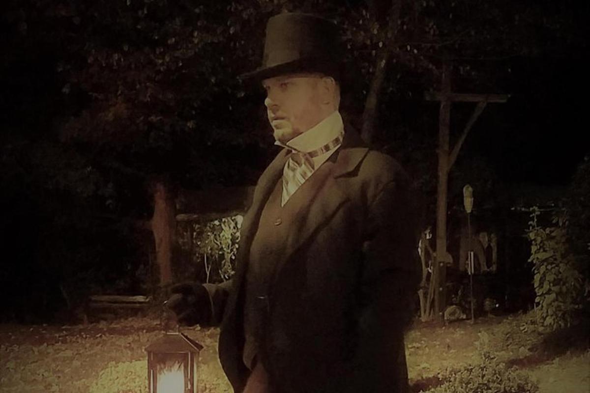 a man in a suit and top hat standing next to a lantern