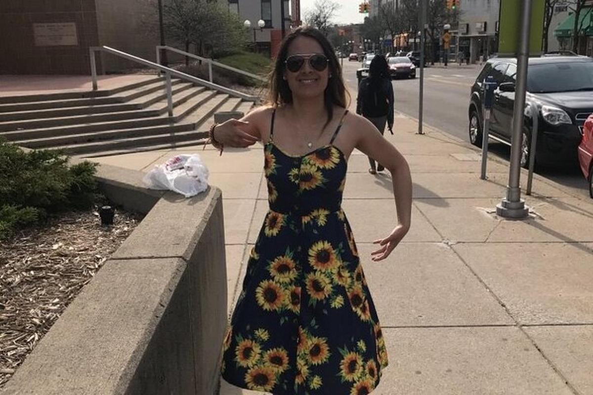 eine Frau in einem geblümten Kleid steht auf einem Bürgersteig