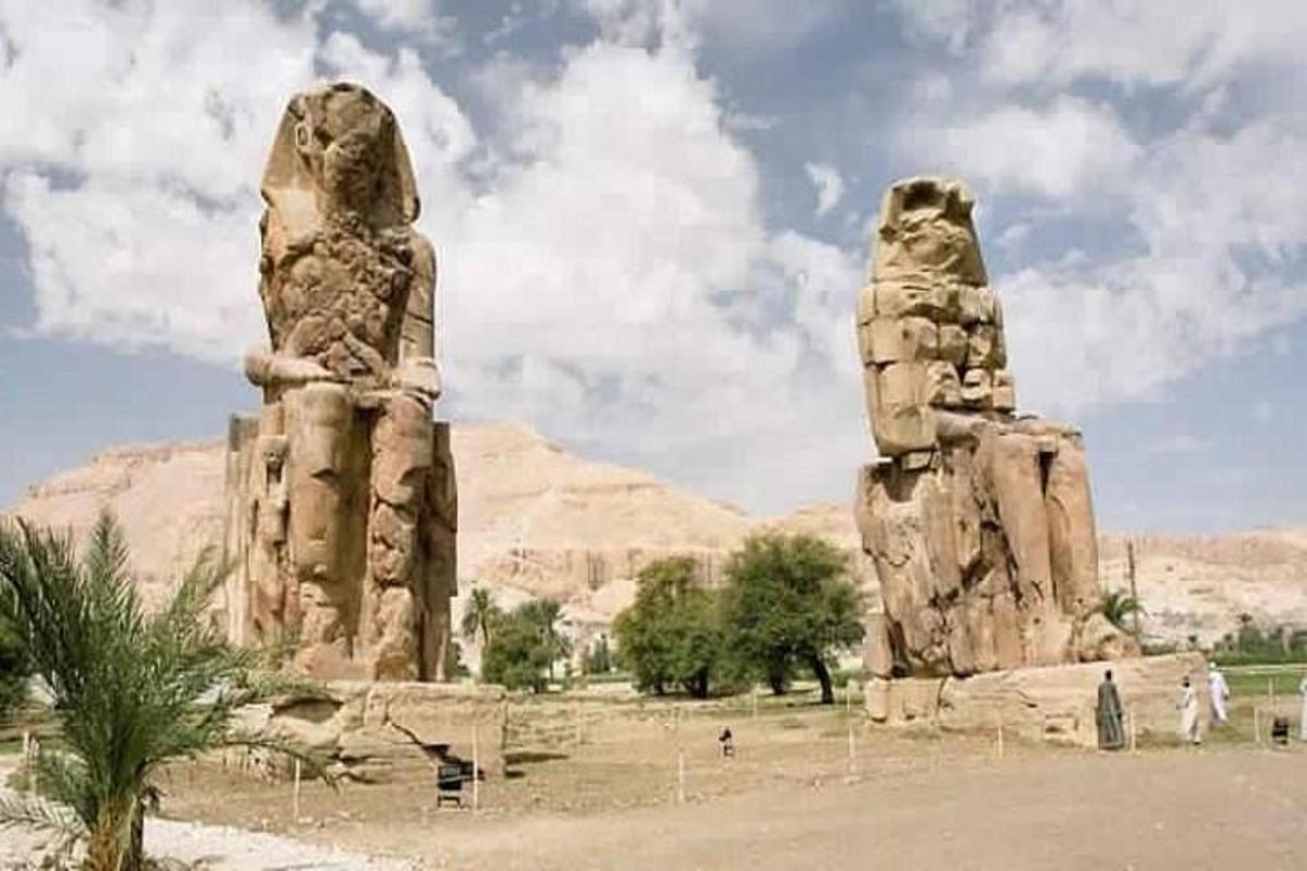 due grandi statue di pietra in un campo con montagne sullo sfondo