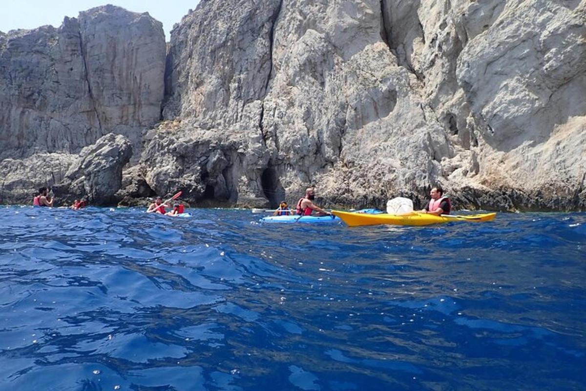un gruppo di persone che fa kayak in acqua vicino a una scogliera