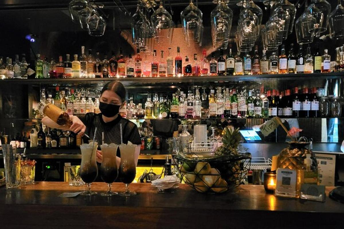 una donna che indossa una maschera mentre prepara un drink in un bar