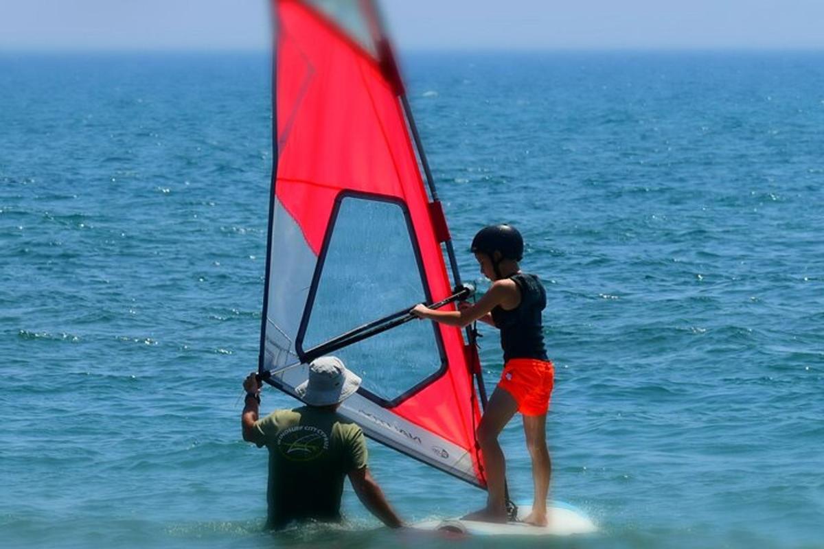 two people on surfboards with a red sail on the ocean