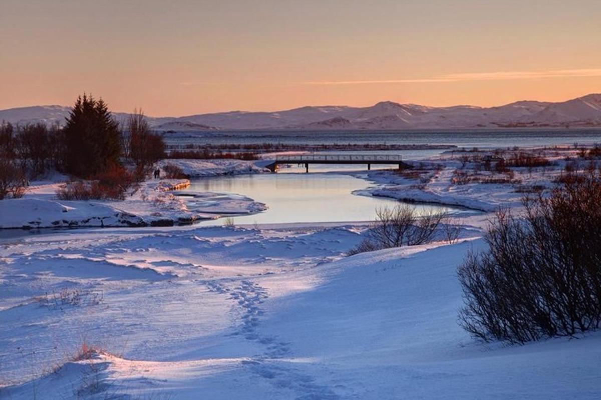 a winter scene of a river with snow and mountains
