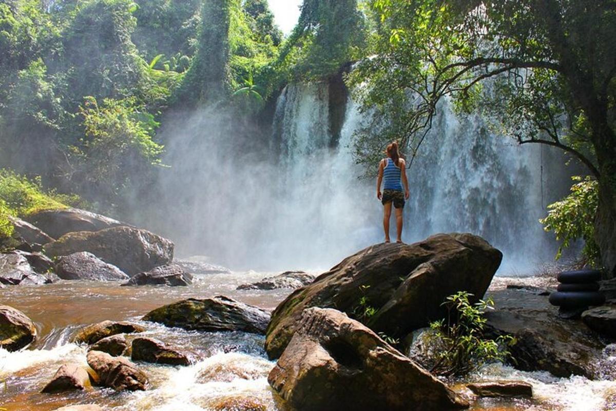 eine Person, die auf einem Felsen vor einem Wasserfall steht