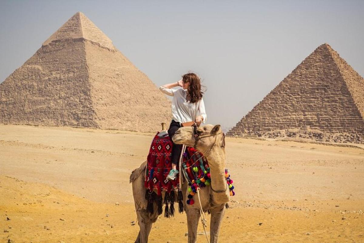 eine Frau, die vor Pyramiden auf einem Kamel reitet