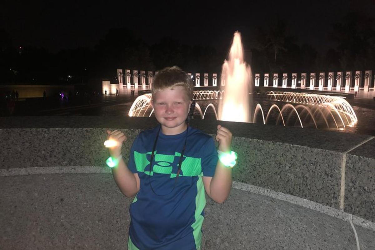 a young boy holding up lights in front of a fountain