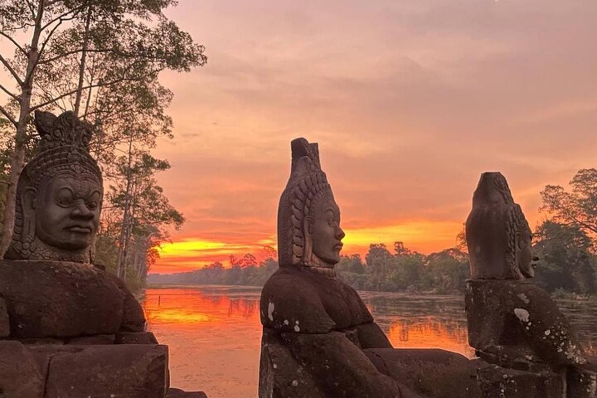 three statues standing in front of a river at sunset