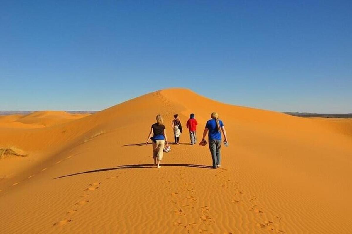 three people walking down a sand dune in the desert