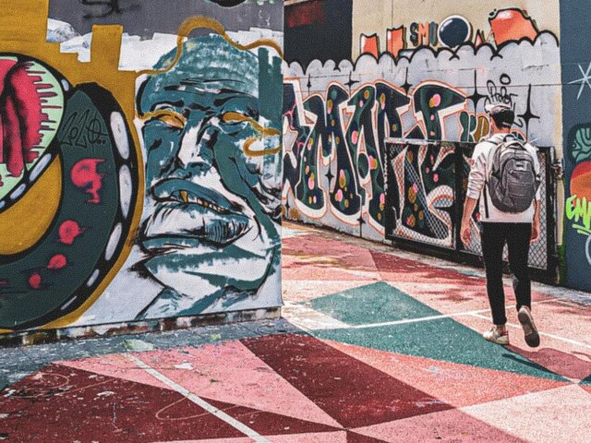 en person med en ryggsekk som går forbi en vegg dekket av graffiti