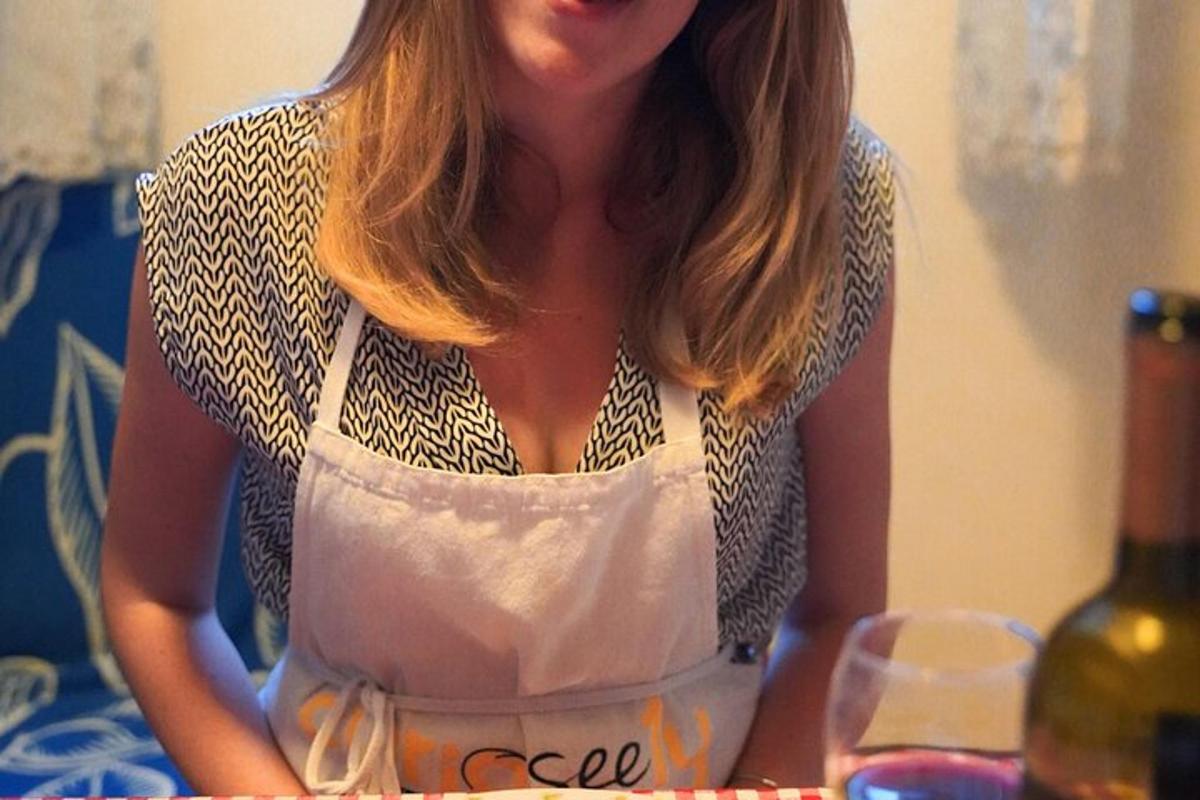 uma mulher de avental sentada à mesa com uma garrafa de vinho