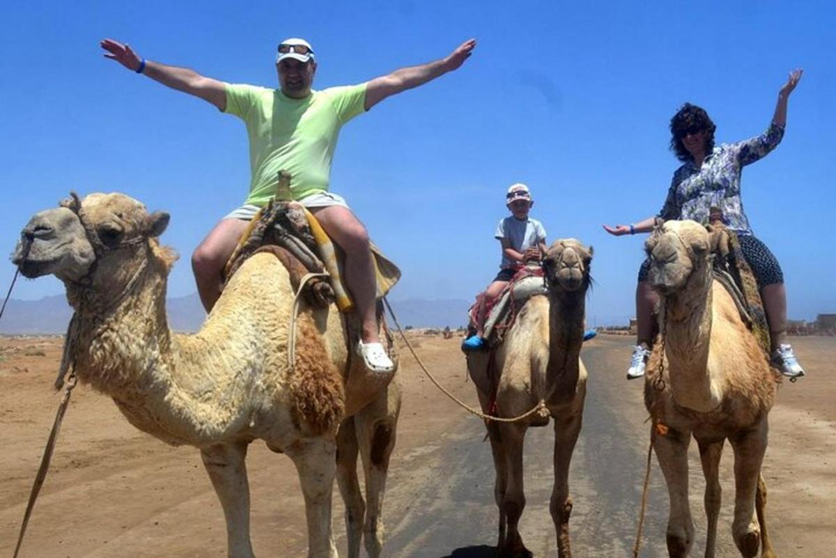 Tres personas viajan en camellos en el desierto.