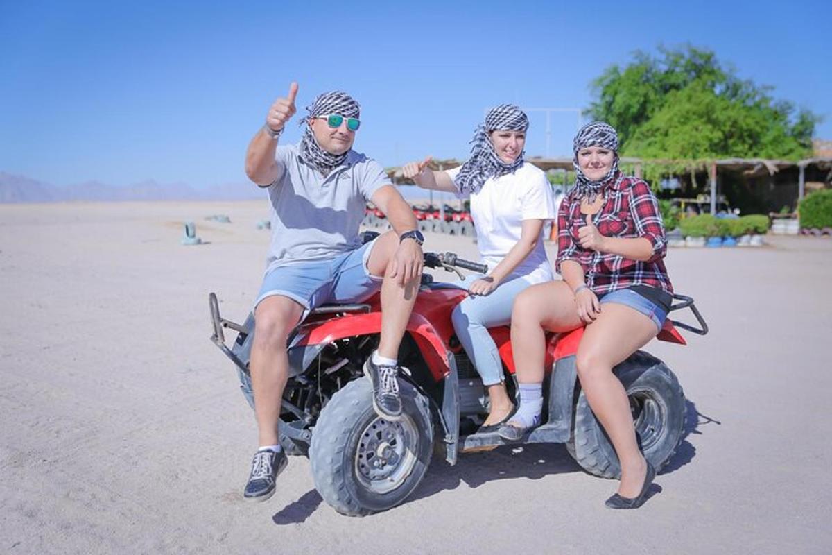 três pessoas sentadas em um quadriciclo na praia