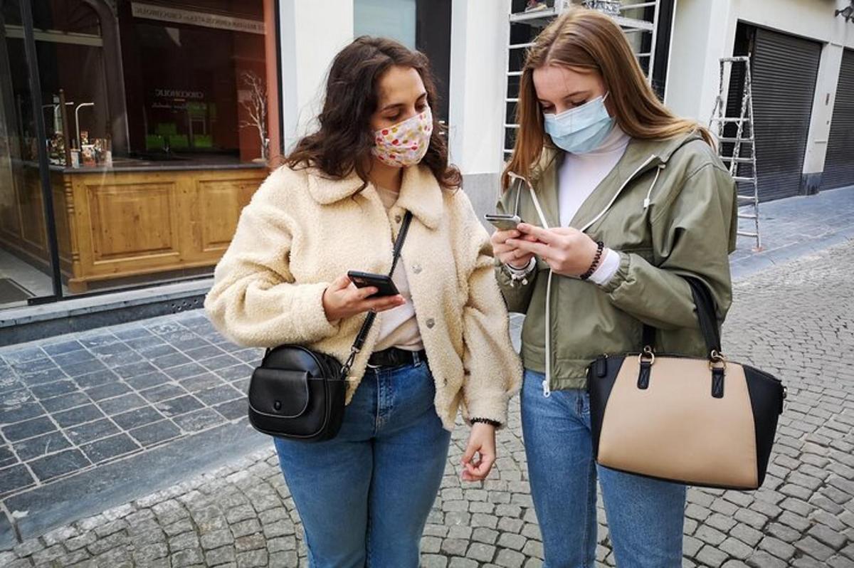 dvě ženy v rouškách jdoucí po ulici s mobilními telefony ve svých rukou