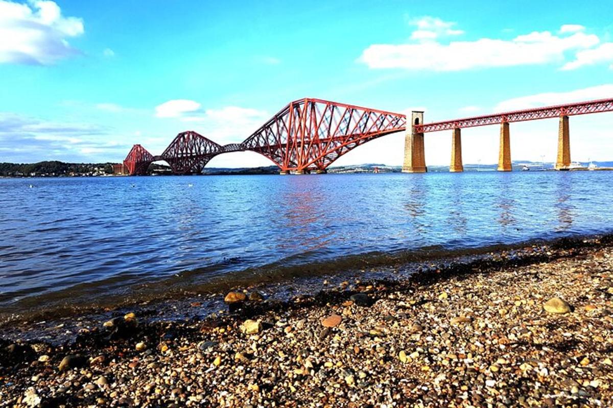 a red bridge over the water with a rocky shore