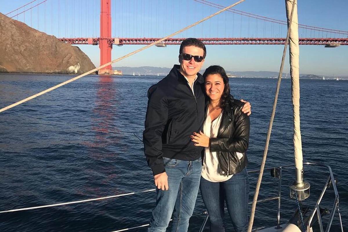 Un hombre y una mujer de pie en un barco frente al puente Golden Gate.