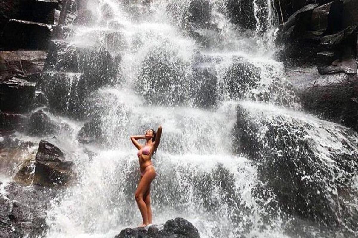 dua wanita berdiri di atas batu di hadapan air terjun