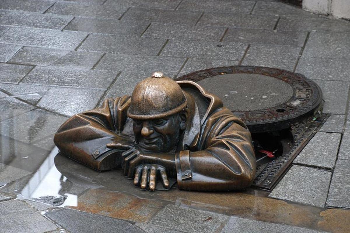 Una estatua de bronce de un hombre tendido en una alcantarilla.