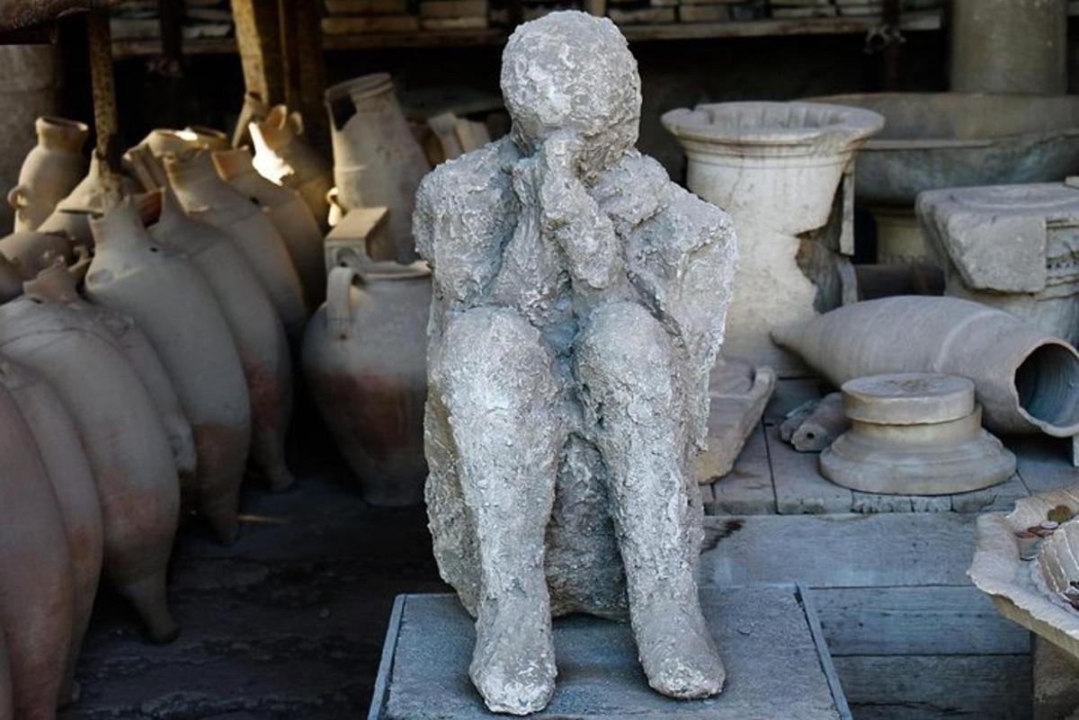 Una estatua de una persona sentada frente a jarrones.