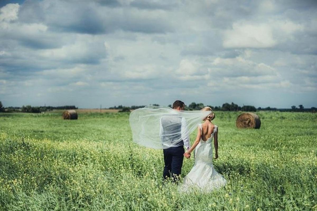 una sposa e uno sposo che camminano in un campo con un velo
