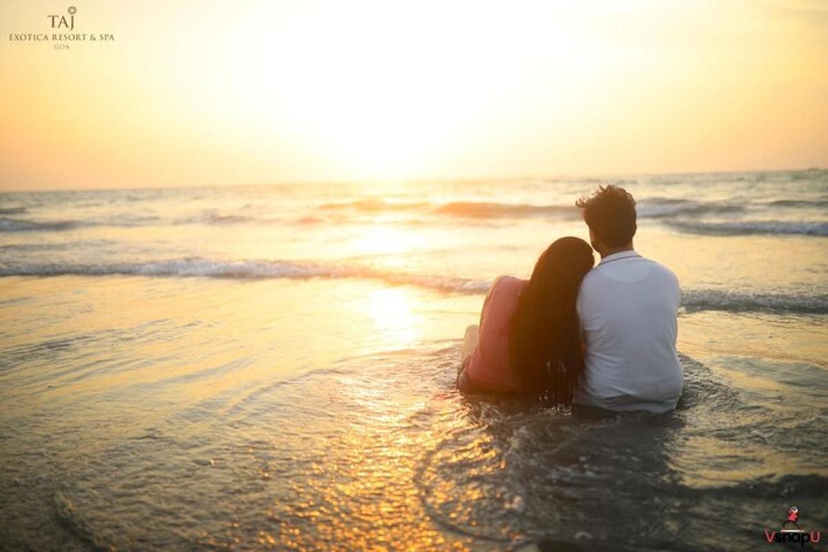 Una pareja sentada en la playa viendo la puesta de sol