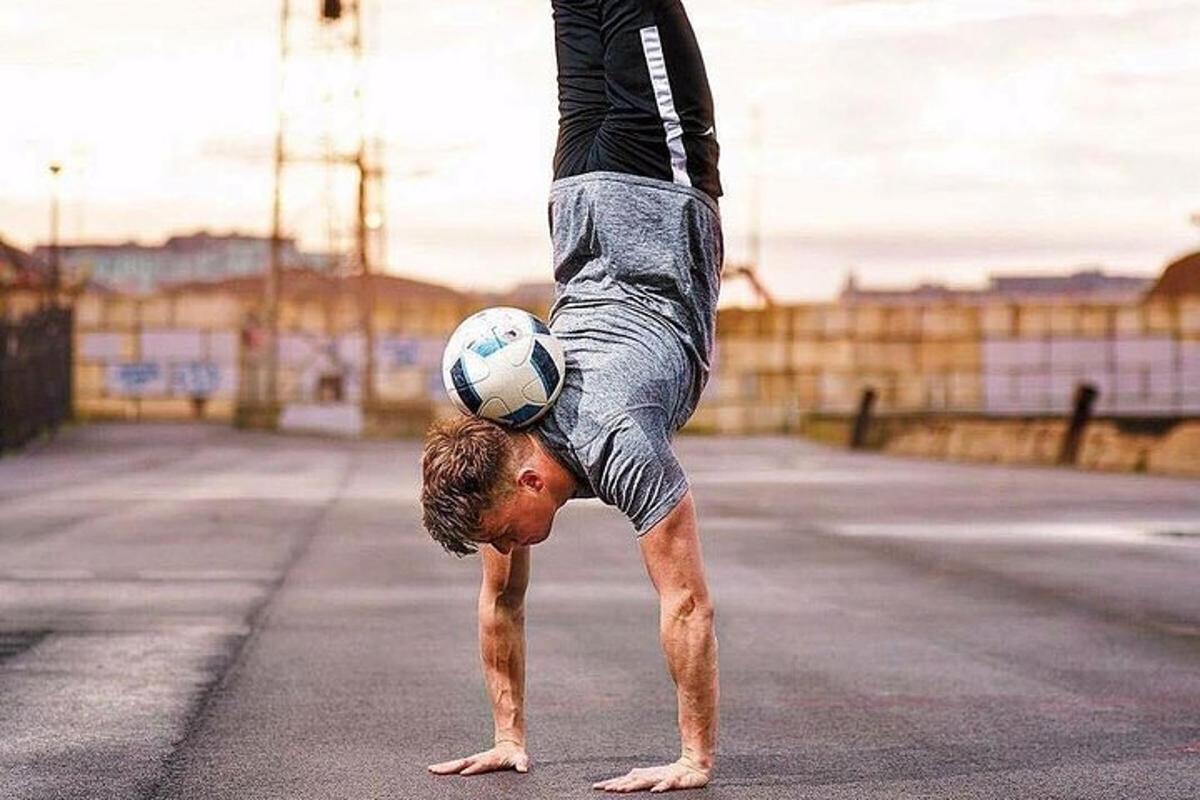 muž dělá stojku s fotbalovým míčem na hlavě