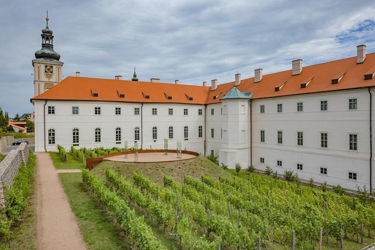 a large white building with an orange roof and a vineyard