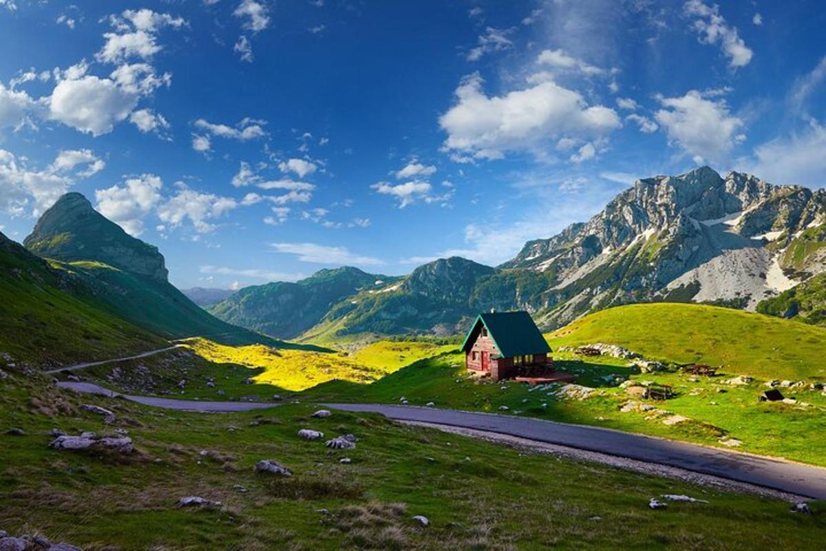 una piccola casa su una collina con una strada e delle montagne